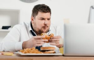 A Man eating his burger while looking on his laptop